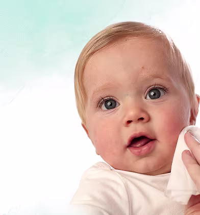 Un prim-plan al feței unui bebeluș în timp ce o mână îi șterge delicat obrazul cu un șervețel Pampers Harmonie Aqua.