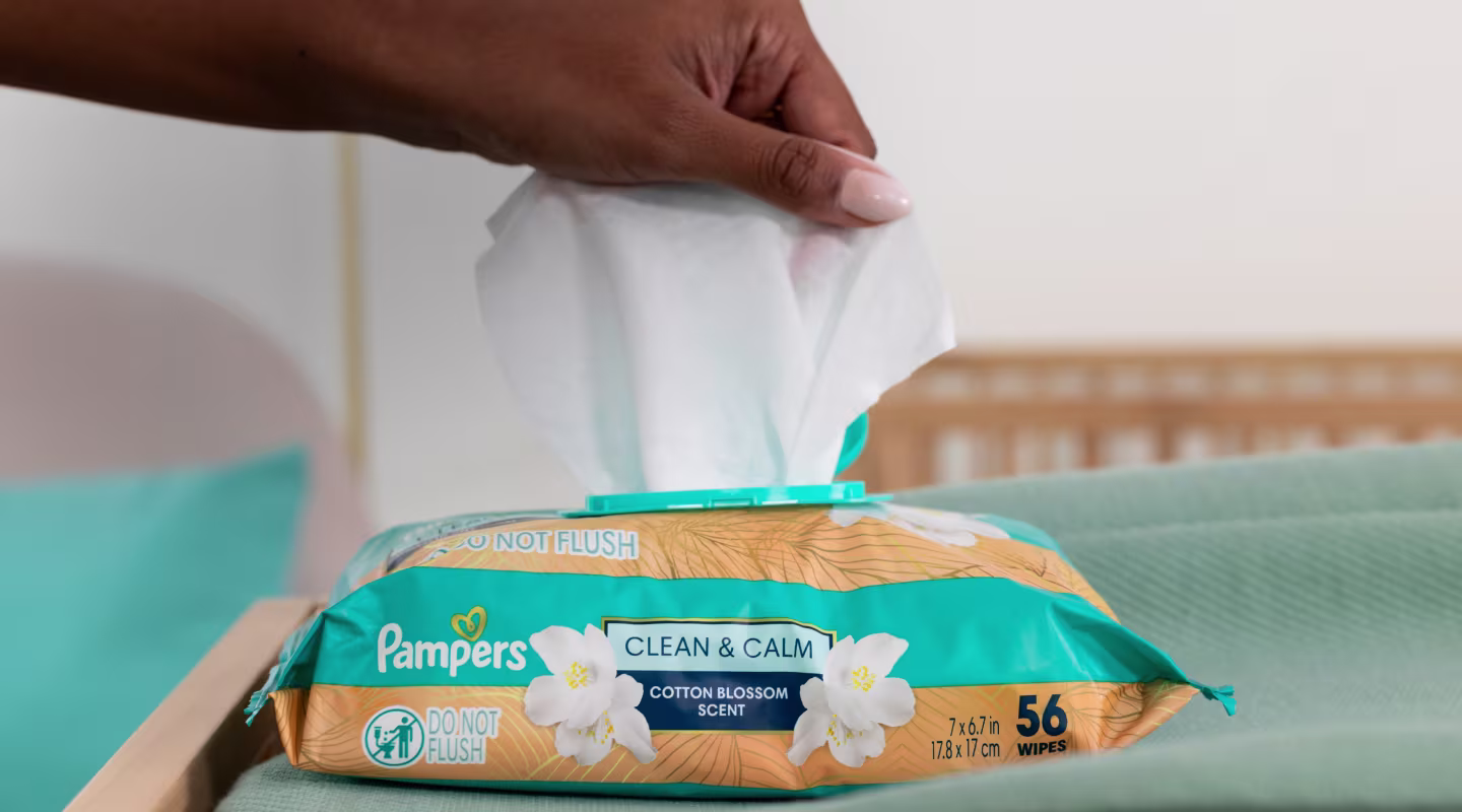 Acercamiento de una mano sacando una toallita Clean and Calm del paquete mientras descansa sobre un cambiador.