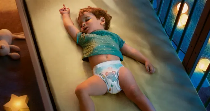 Ein schlafendes Baby liegt in einem Babybettchen und trägt eine Pampers Baby-Dry Windel.