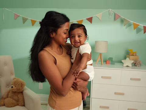 Mamá sosteniendo al bebé en el cuarto de bebé con una bandera decorativa y cajoneras al fondo