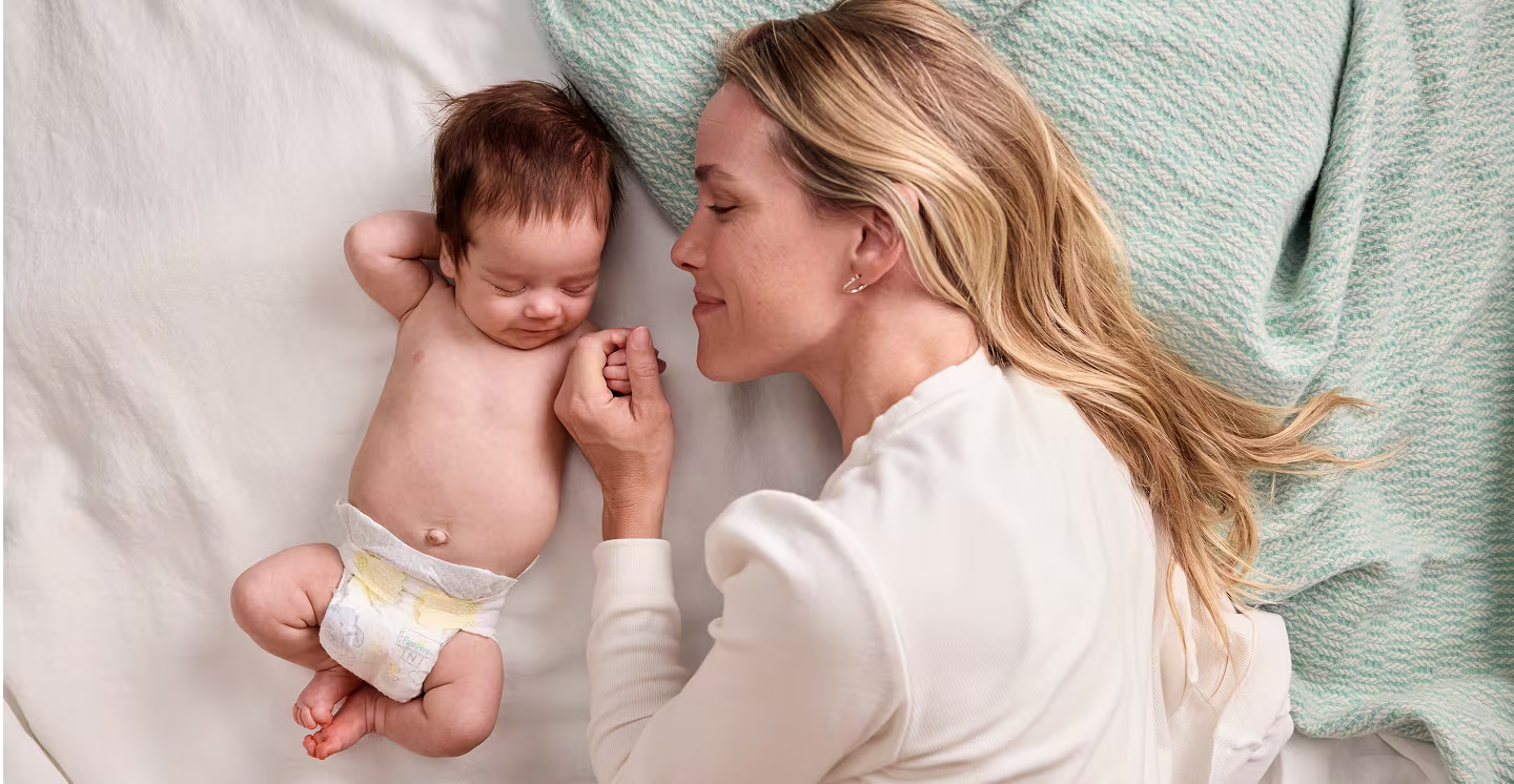 Mamá acostada con el bebé que lleva un pañal Pampers