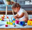 Toddler in white shirt plays with colorful toys on a soft rug, engaging in fun and educational playtime indoors.