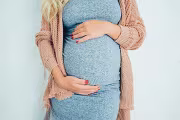 Pregnant woman in a cozy sweater gently cradling her belly.