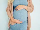 Pregnant woman in a cozy sweater gently cradling her belly.