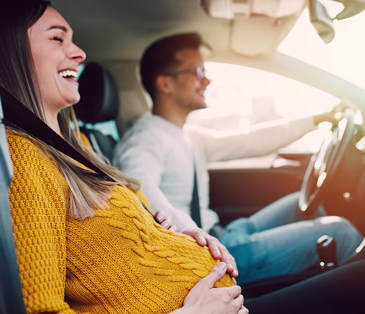 Pregnant woman smiling in car with partner on a sunny day.