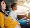 Pregnant woman smiling in car with partner on a sunny day.