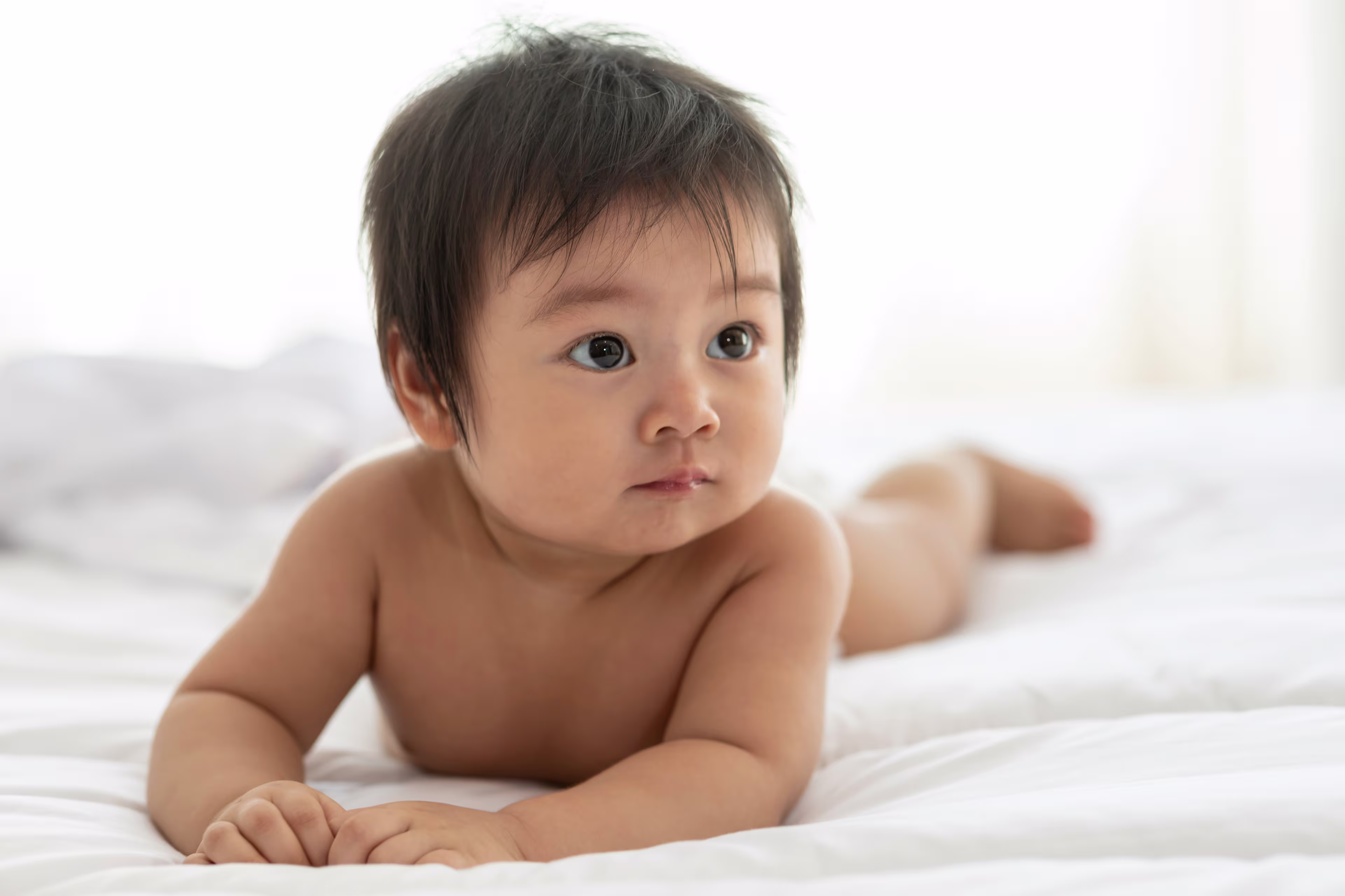 Bebé acostado boca abajo sobre una cama, mirando hacia un lado en un ambiente luminoso.