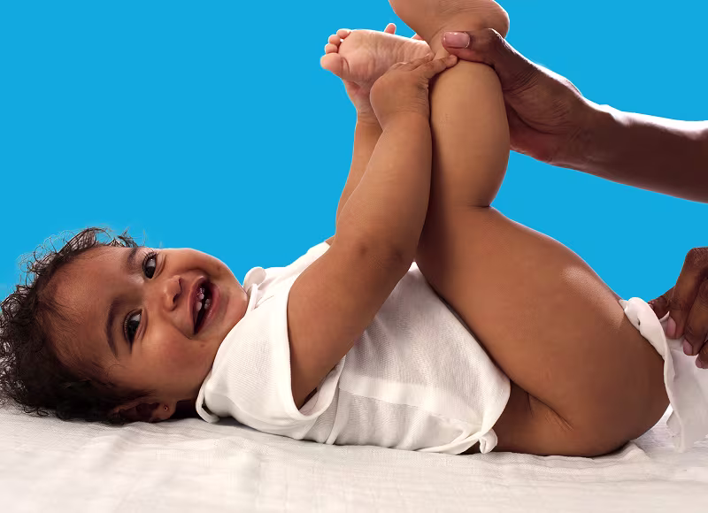 Un bebé está tumbado de espaldas sobre una superficie blanca, levantando los pies mientras un padre utiliza una toallita para limpiar el trasero del bebé.