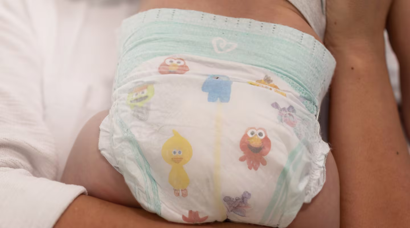 Un padre amoroso sostiene suavemente a su bebé en sus brazos, mostrando el ajuste perfecto del pañal Pampers, diseñado para brindar máxima comodidad y protección.