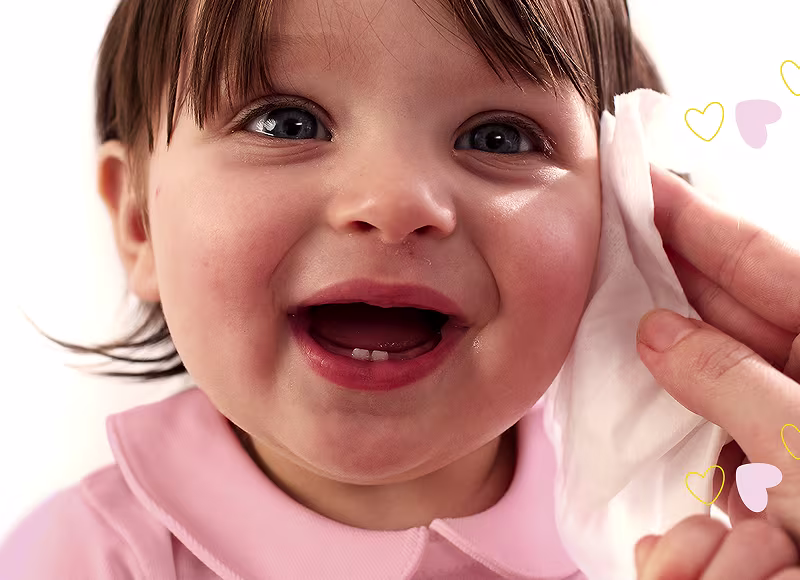 Un gros plan du visage d’un bébé, tandis qu’une main nettoie doucement la joue avec une lingette Pampers Sensitive.