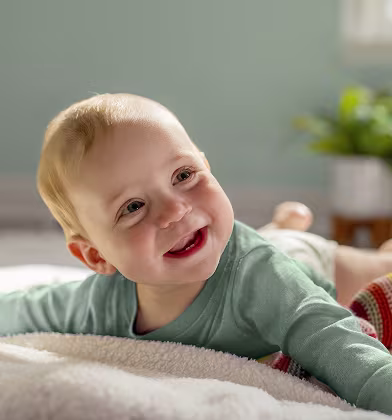 Baby laying on their belly doing tummy time and smiling while wearing a teal onesie Baby laying on their belly doing tummy time and smiling while wearing a teal onesie