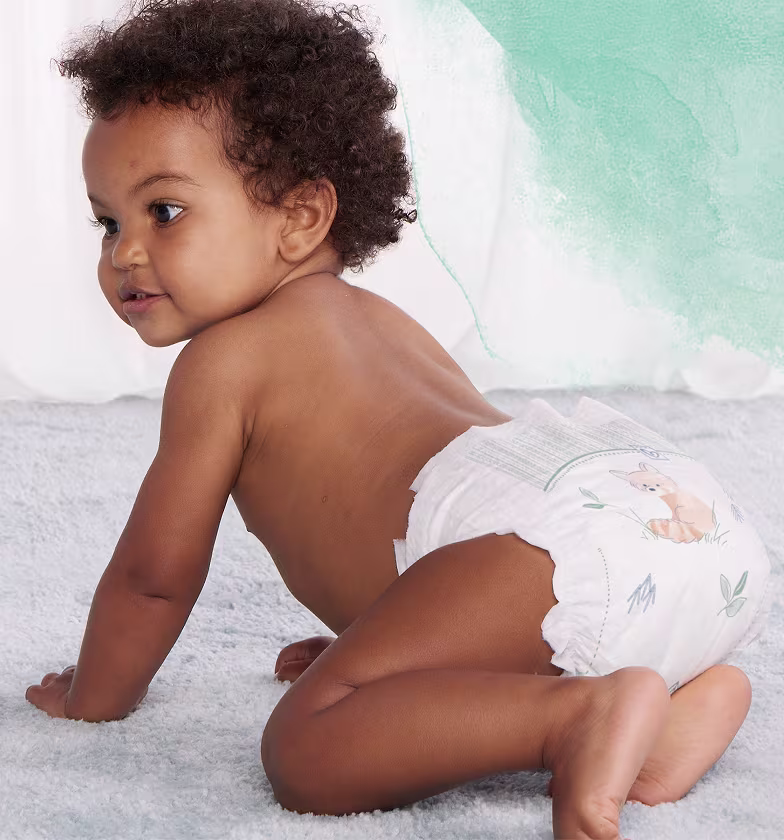 Een baby met een Pampers-luier zit op handen en knieën en kijkt over zijn rechter schouder.