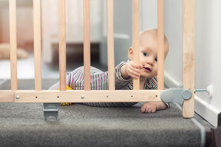 Bebeluș care se târăște în fața unor balustrade din lemn.