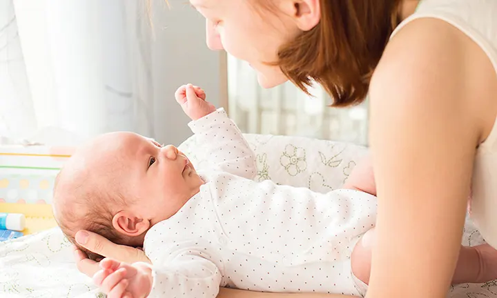 Mother interacting with her baby on a changing table, showcasing essential items for newborn care