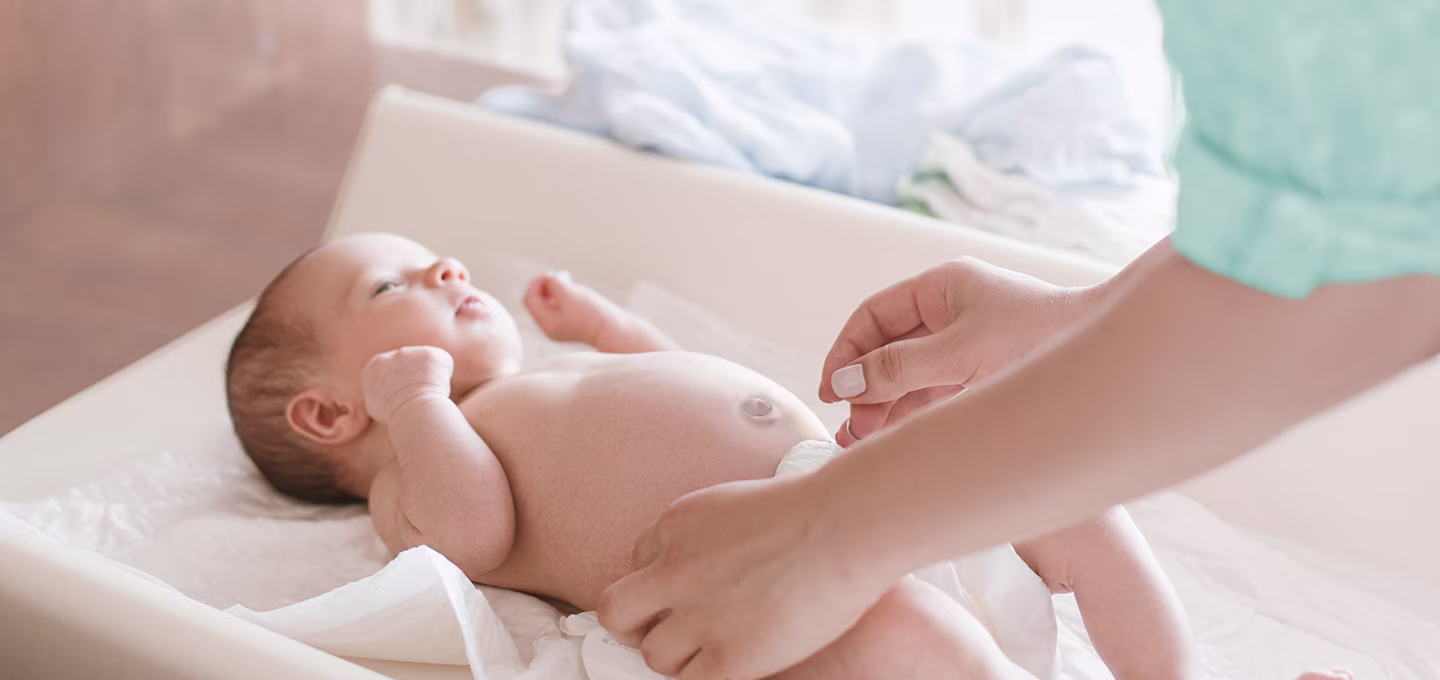 A newborn baby lying on a changing pad while their caregiver changes their diaper