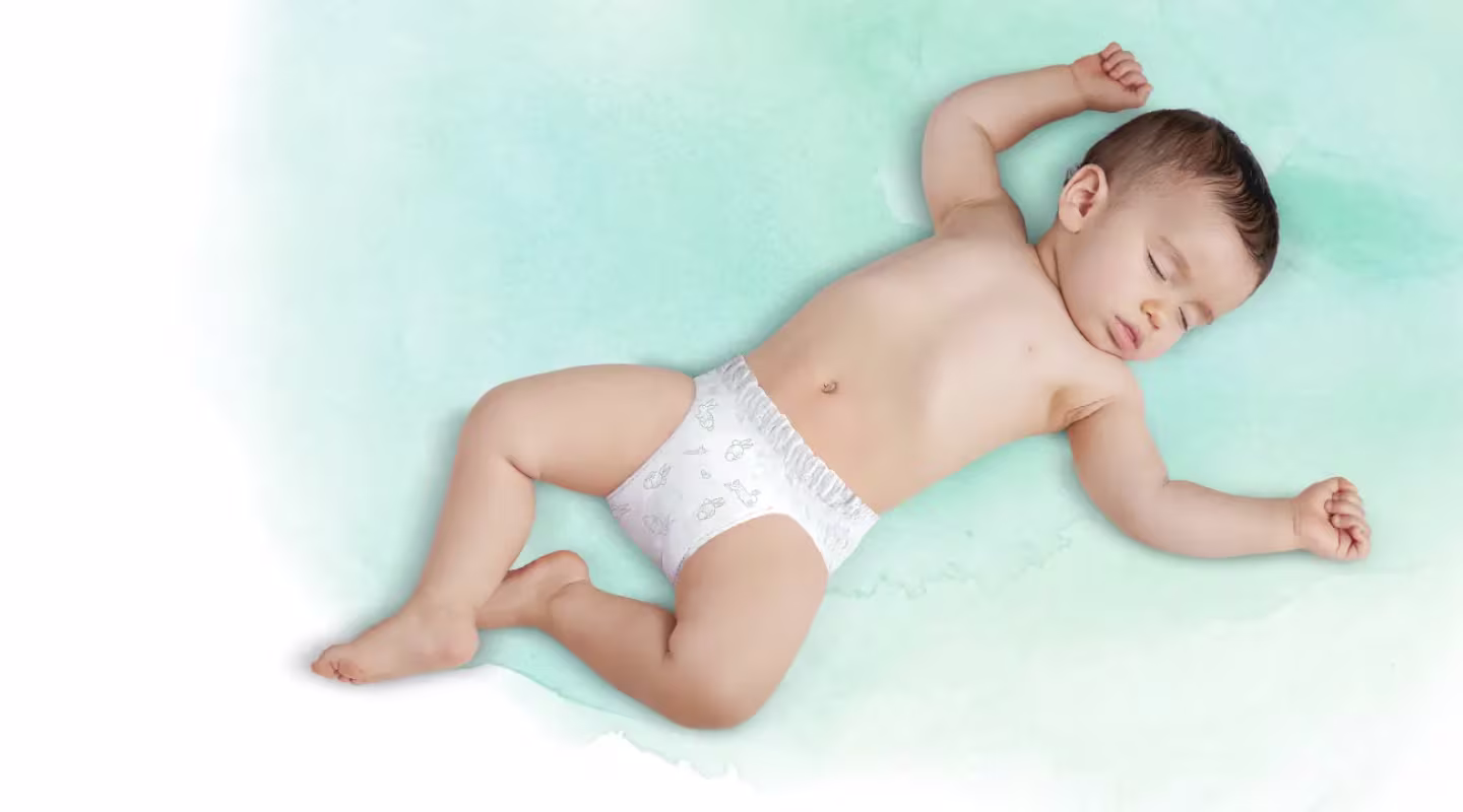 A baby sleeps soundly on their back, wearing a white nappy pant with blue bunny and carrot designs.
