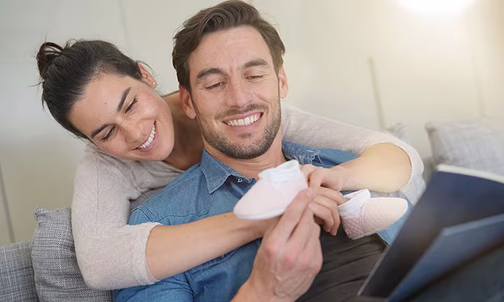 Manos de una pareja sosteniendo unos calcetines de bebé blancos, una idea tierna para anunciar un embarazo.