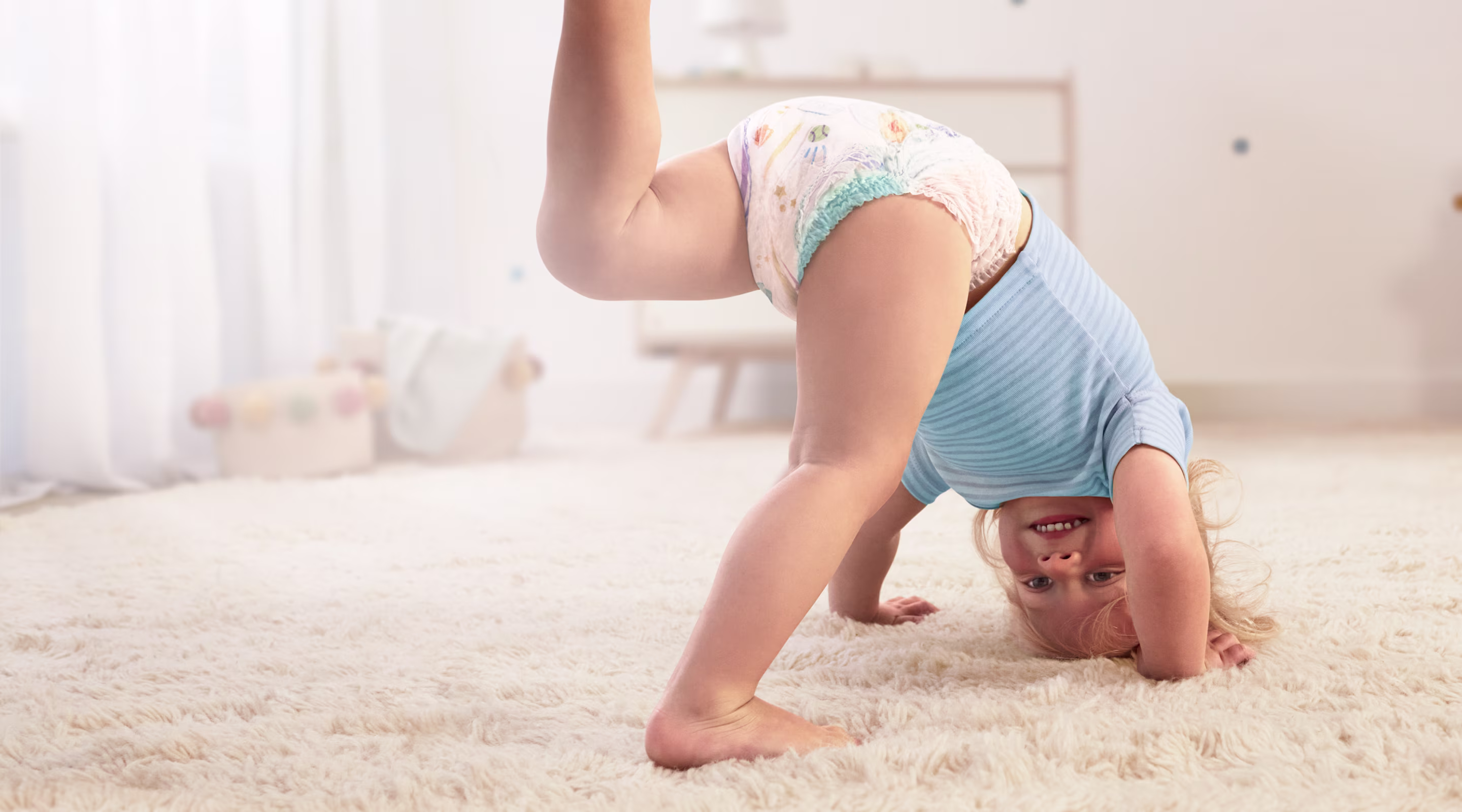 Ein Babys, das eine Pampers® Baby-Dry™ Pants trägt, macht einen Handstand und streckt ein Bein in die Luft.