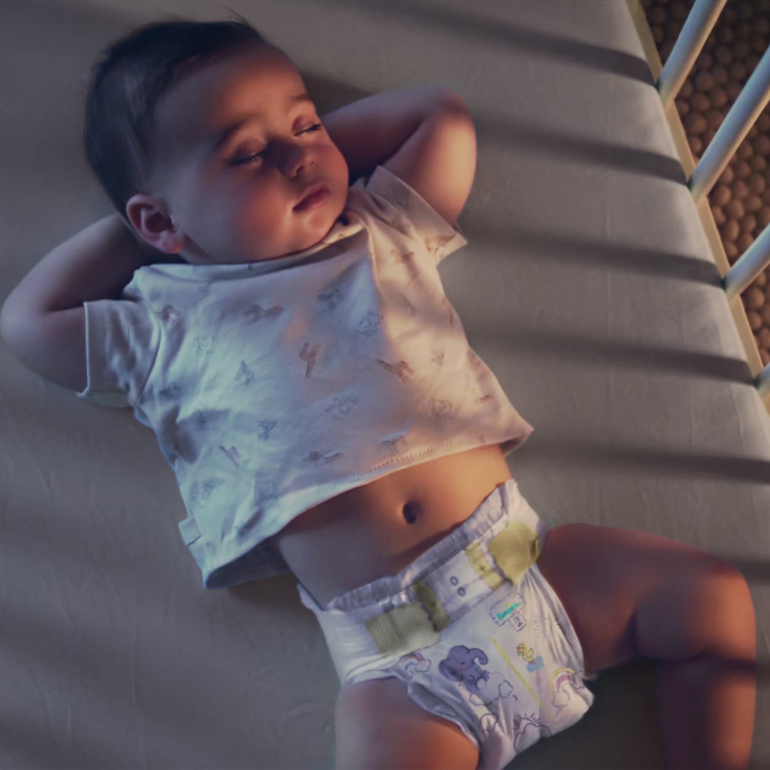 Baby sleeping peacefully in the crib wearing Pampers Swaddlers and a gray shirt