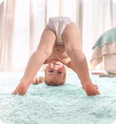 Een baby met een Pampers® Premium Protection™ Pants kijkt vrolijk naar de camera en leunt op een gestreept kussen.