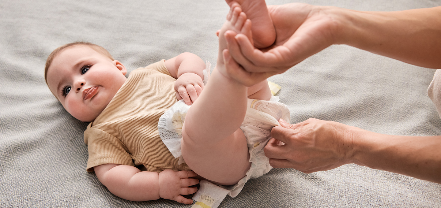 An adult’s hands gently fastening a clean diaper on a lying baby during a diaper change, showing proper placement and technique