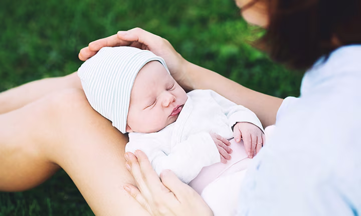 Neugeborenes liegt auf Mutters Beinen