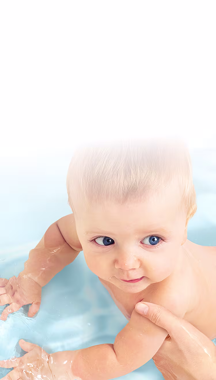 Eine Draufsicht auf ein Baby, das sanft von der Hand eines Erwachsenen in klarem, blauem Wasser gestützt wird.