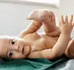 Baby lying on a green blanket during a diaper change as a caregiver prepares supplies, illustrating gentle home care.