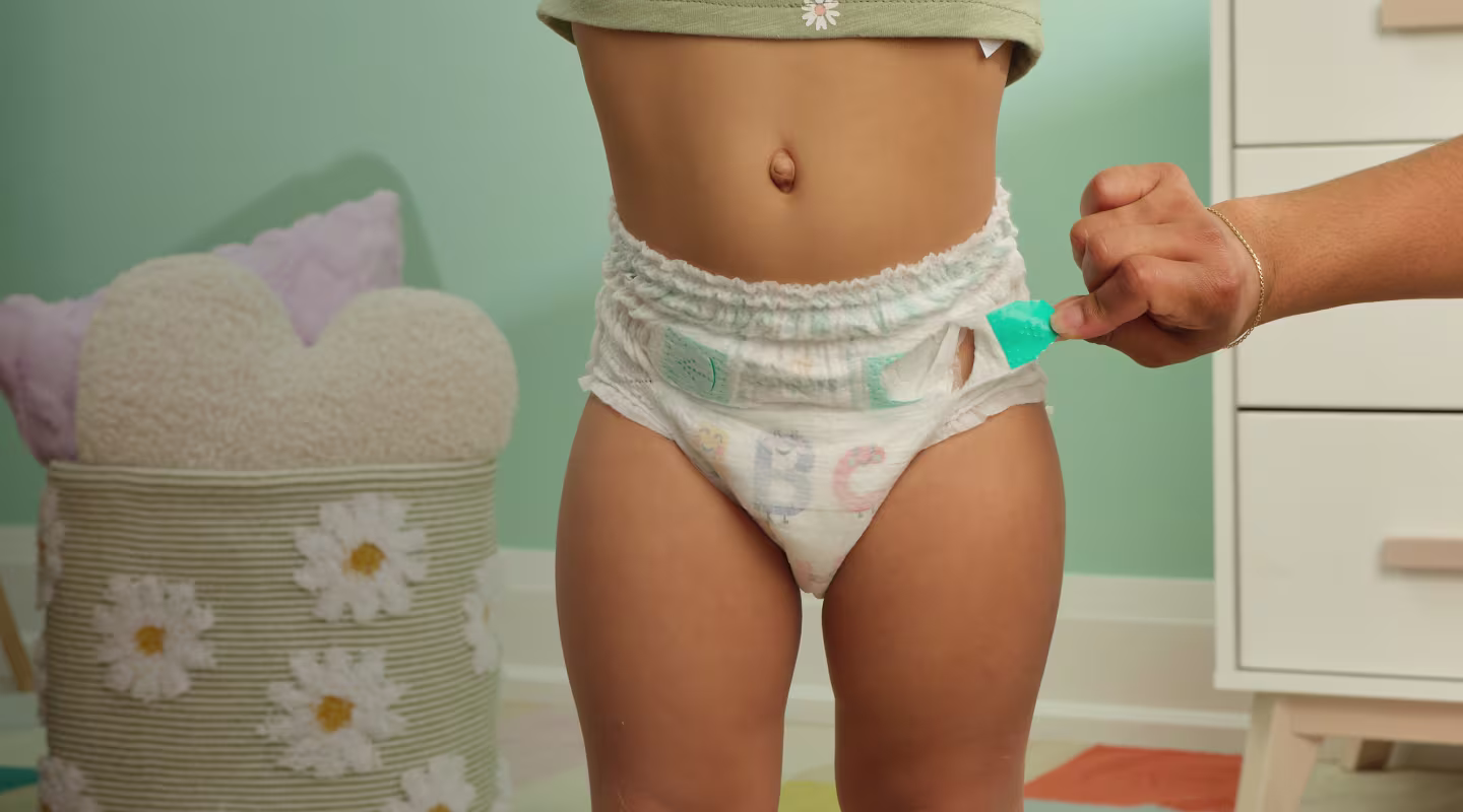 La mano de un papá jalando las pestañas EZ off de un pañal Pampers Cruisers 360 pull on en un niño pequeño de pie