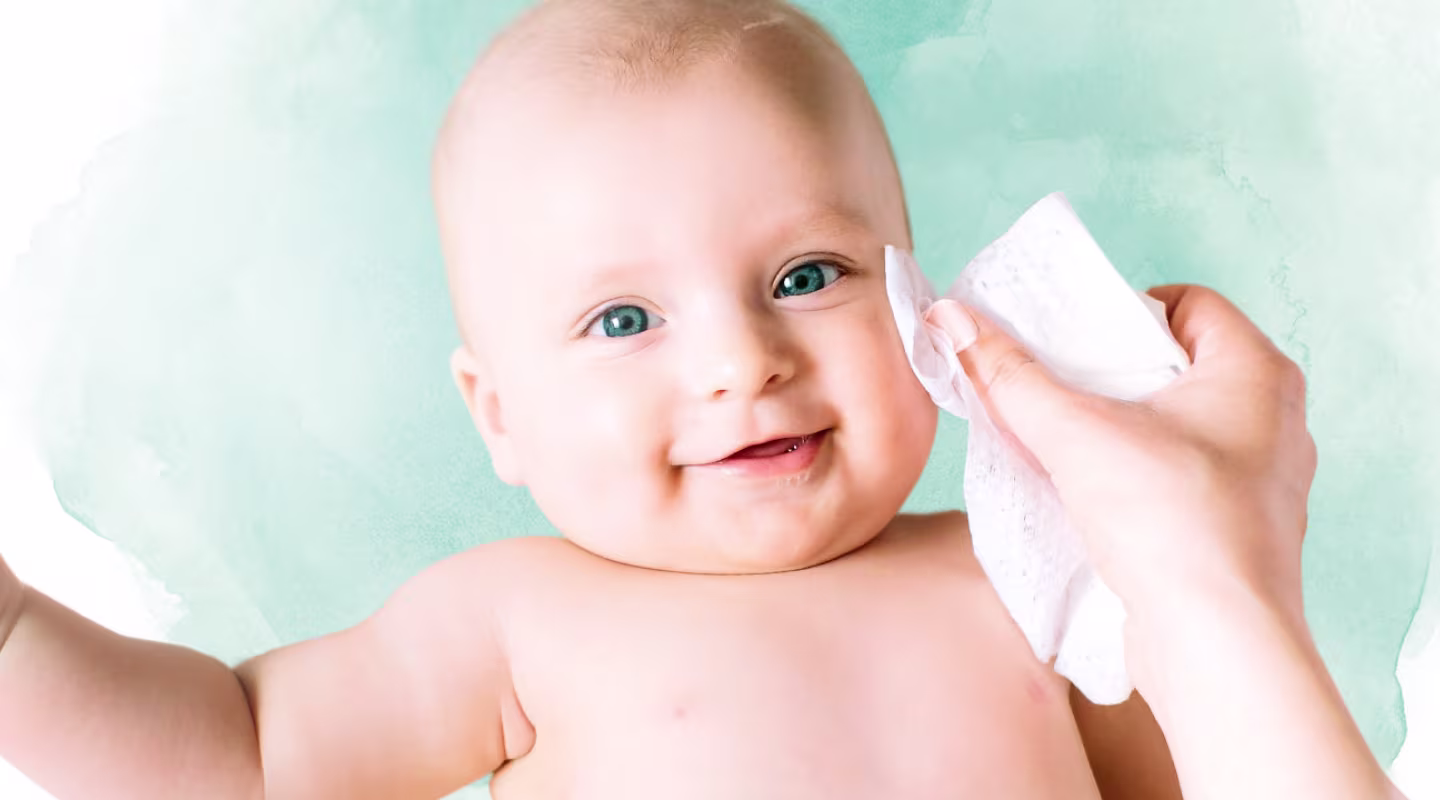 Prim-plan pe fața unui bebeluș, în timp ce o mână îi șterge delicat obrazul cu un șervețel Pampers Harmonie Protect & Care.