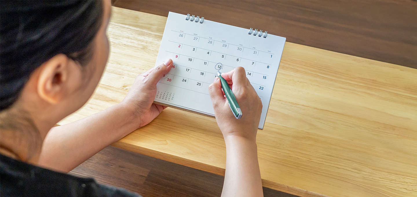 Personne assise à une table, marquant une date sur un calendrier posé devant elle.