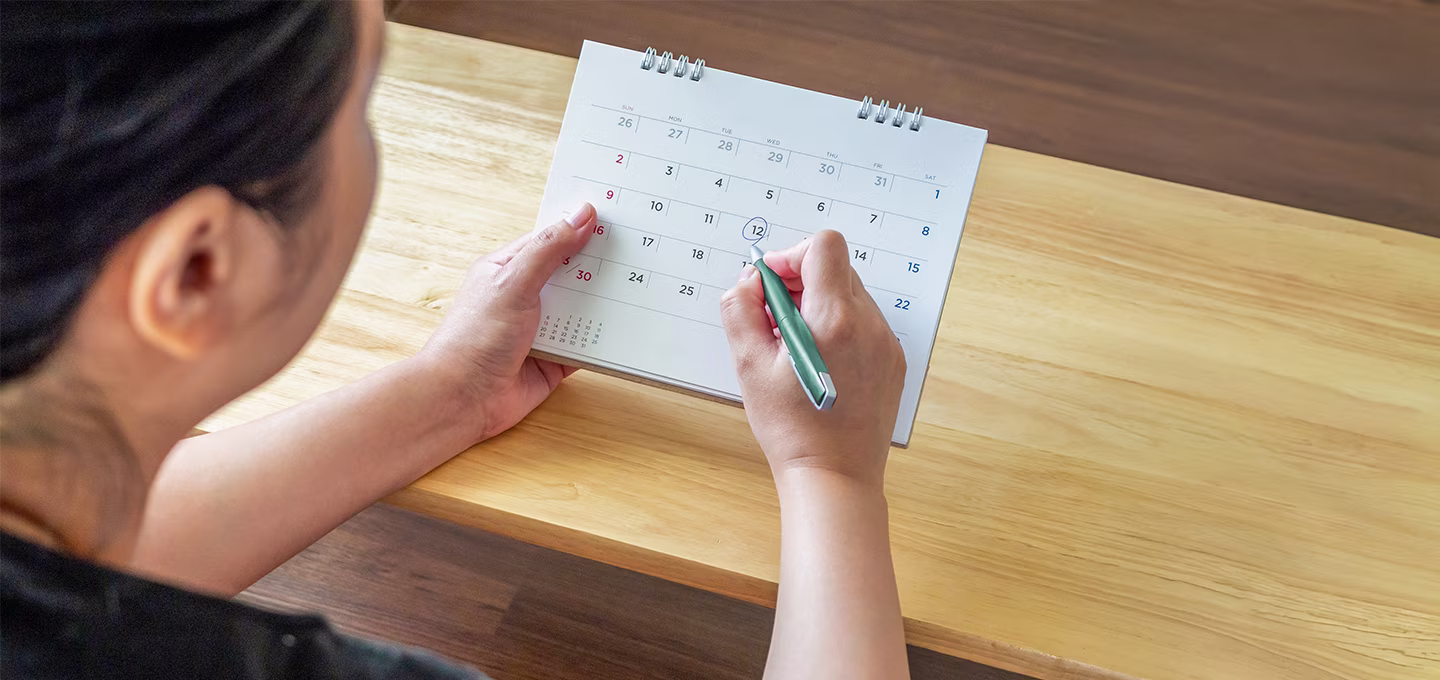 Personne assise à une table, marquant une date sur un calendrier posé devant elle.