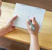 Personne assise à une table, marquant une date sur un calendrier posé devant elle.
