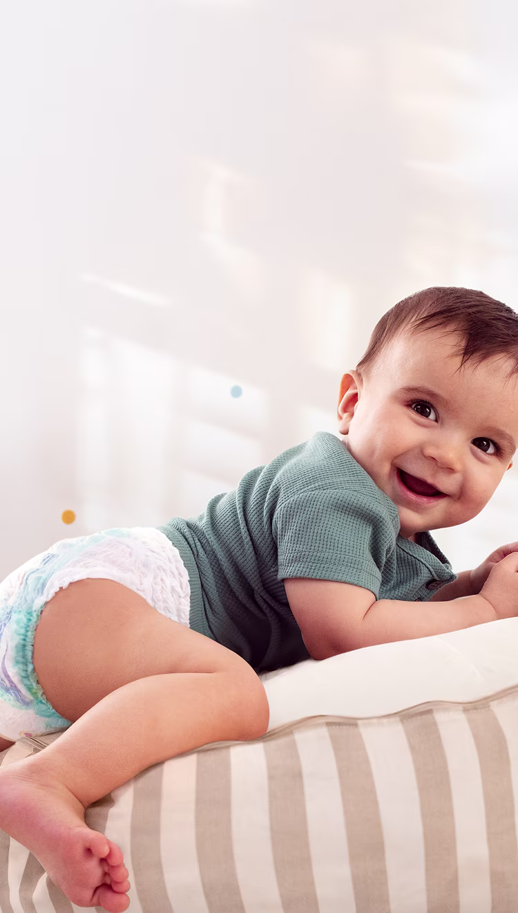 Ein Baby, das eine Pants trägt, lächelt in die Kamera, während es auf dem Bauch auf einem gestreiften Kissen liegt.
