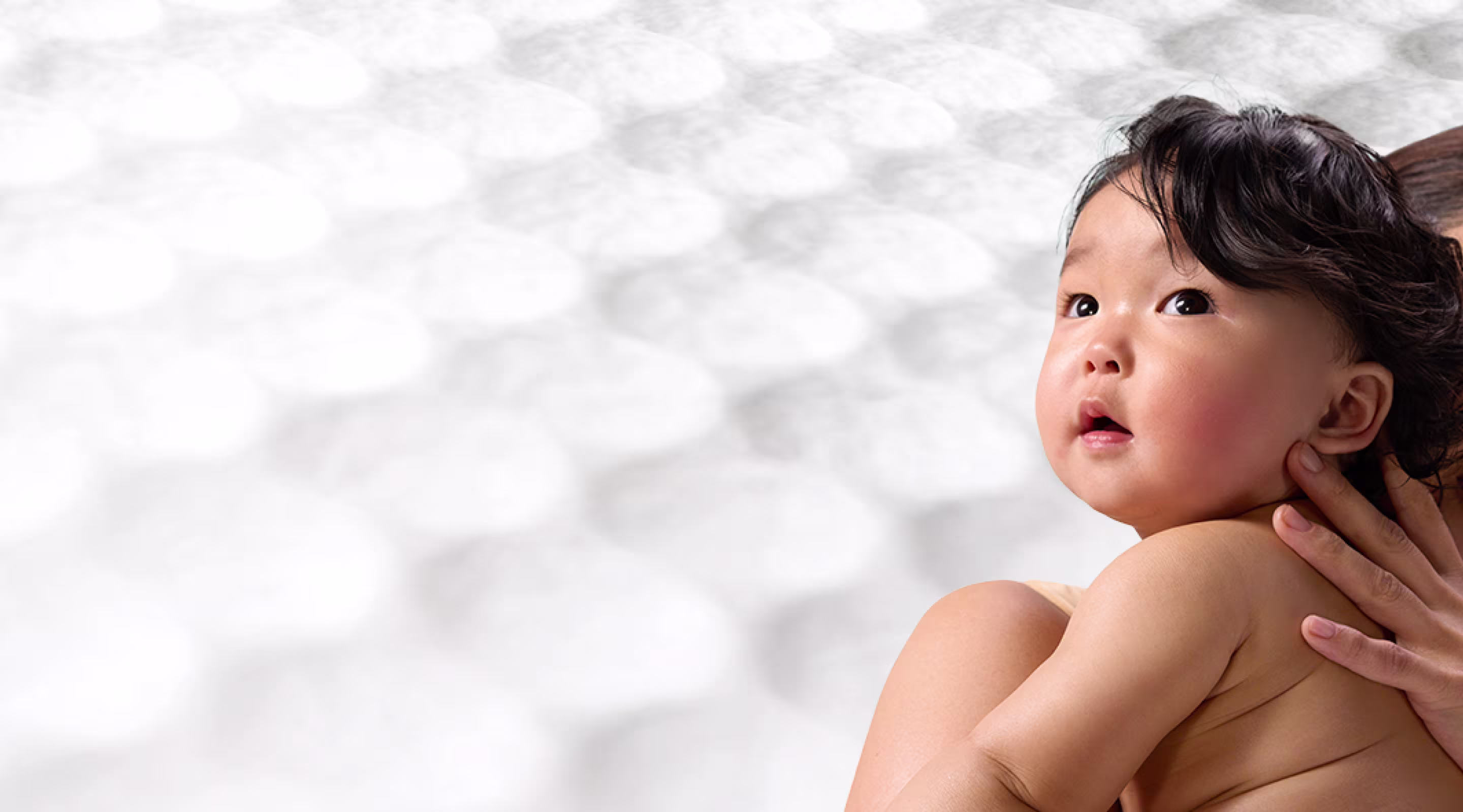 Eine Mutter hält ein Baby auf dem Arm, der Hintergrund zeigt die Waben-Struktur der Pampers® Aqua Soft Touch Feuchttücher