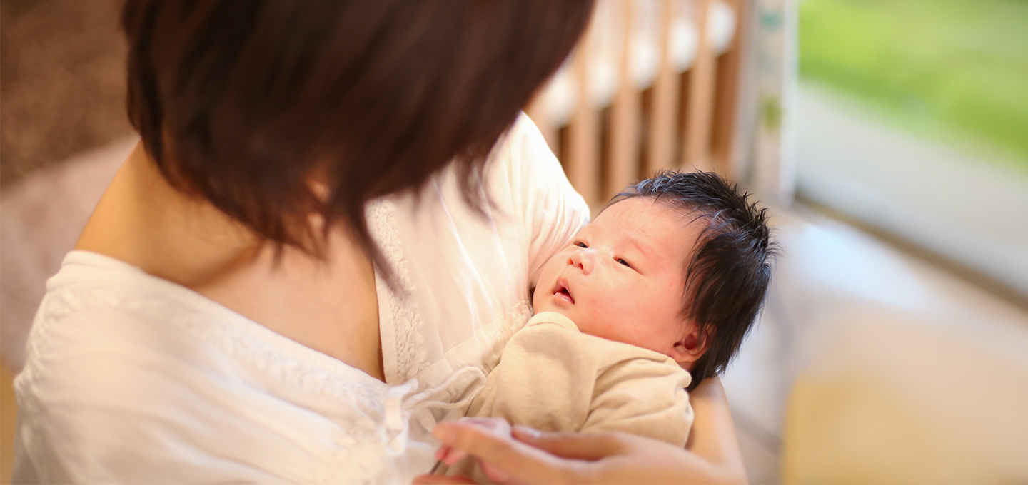 Un adulte tient un nouveau-né dans ses bras, dans une pièce lumineuse.