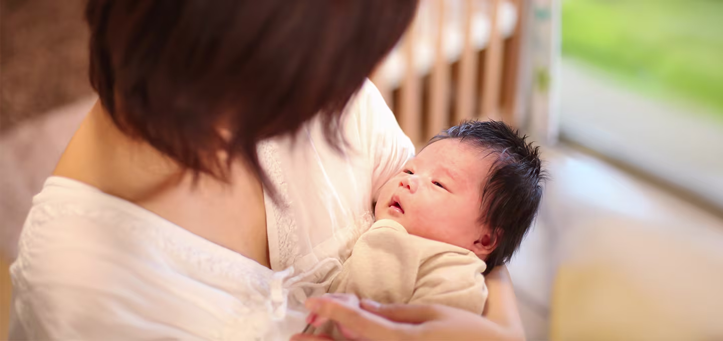 Un adulte tient un nouveau-né dans ses bras, dans une pièce lumineuse.