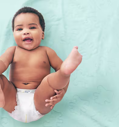 A baby wearing a Pampers nappy with a wide smile lying on his back with legs raised A baby wearing a Pampers nappy with a wide smile lying on his back with legs raised