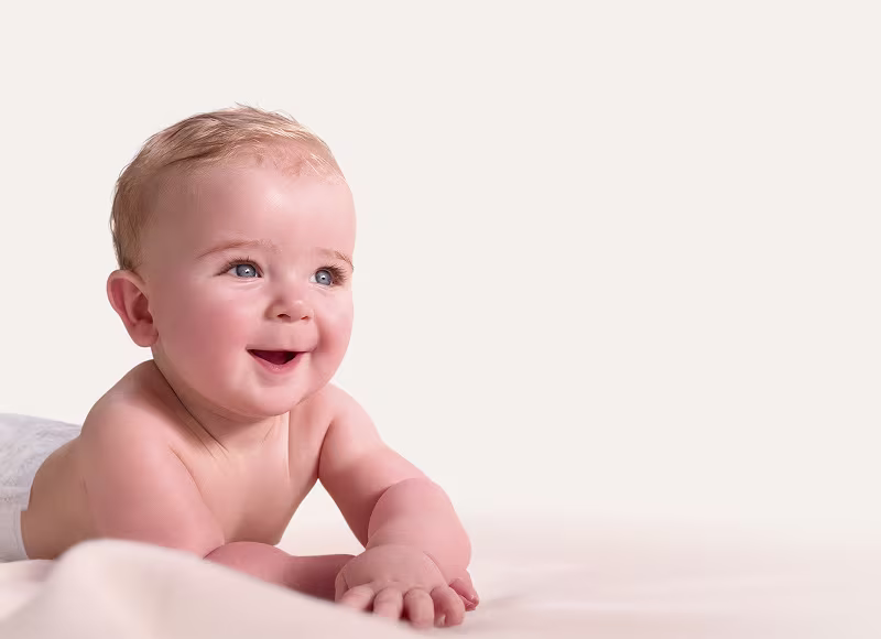 Un bebé feliz con ojos azules está sonriendo y tumbado sobre una manta blanca.