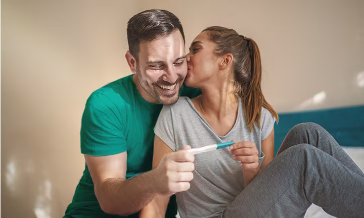Couple joyeux regardant un test de grossesse positif assis dans la chambre