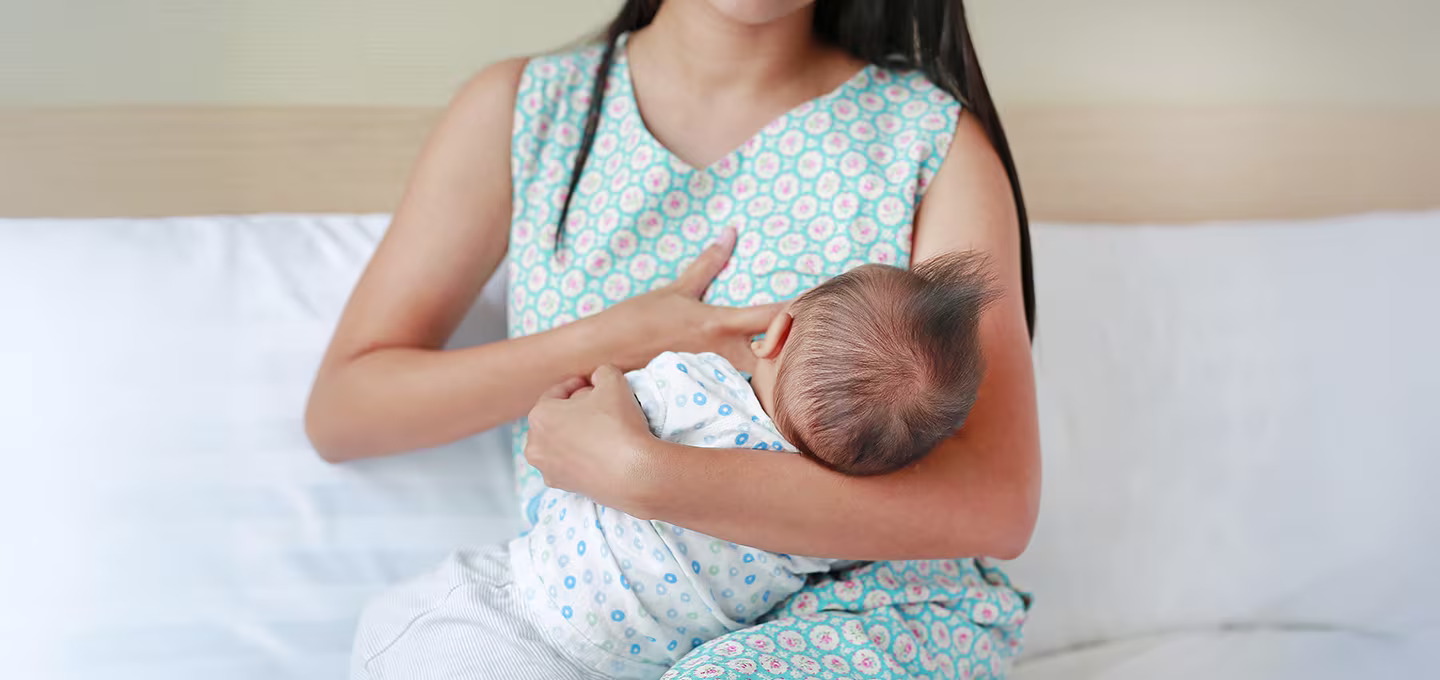 Photo d’une mère allaitant son bébé, assise sur un lit, tenant son nourrisson contre elle pendant qu’il tète.