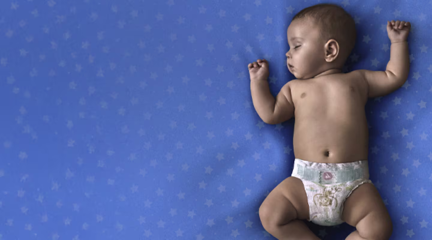 Un bebé que lleva un pañal Dodot, duerme de espaldas sobre una manta verde azulado.