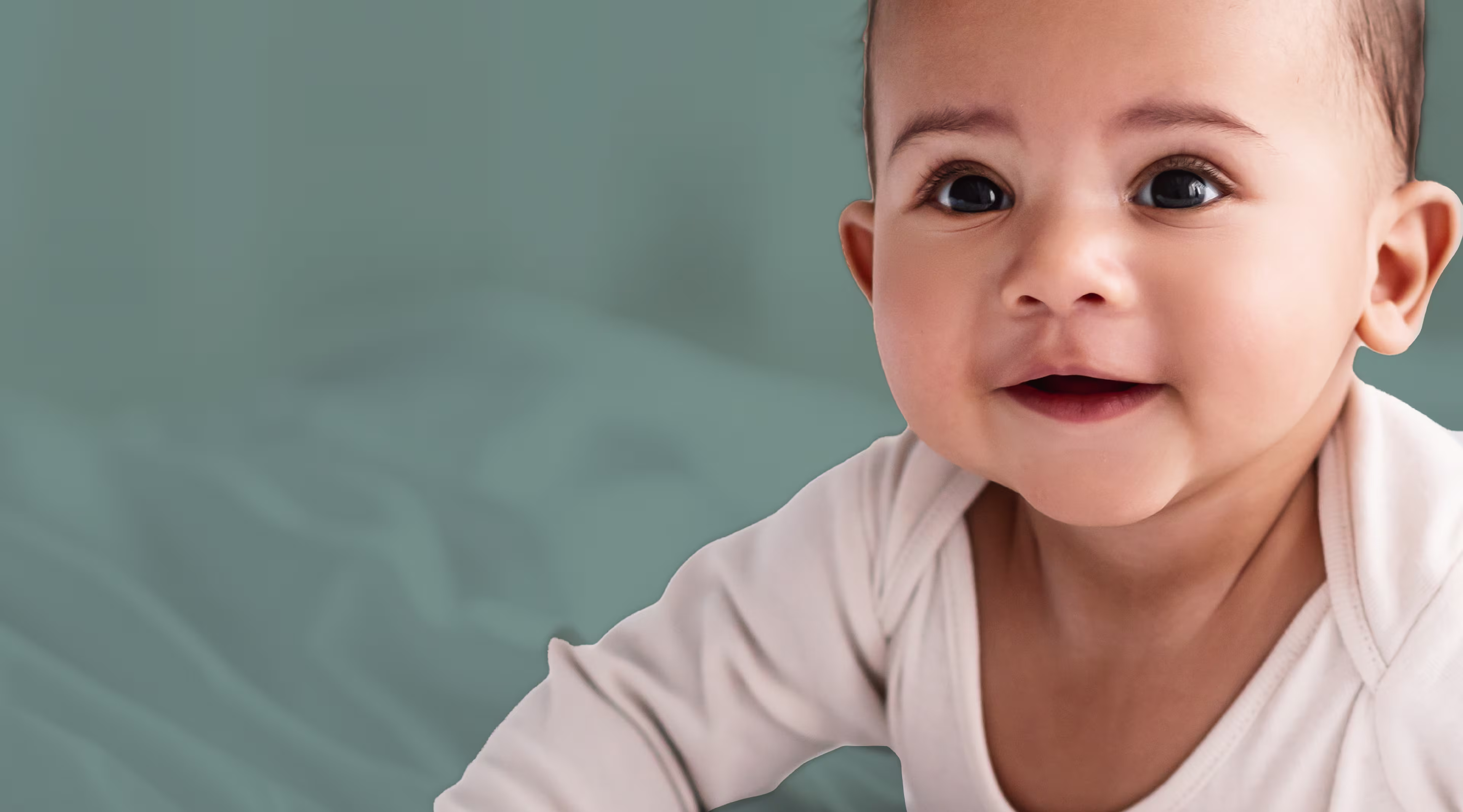 Close up of baby laying on stomach smiling and wearing a cream onesie with sage background