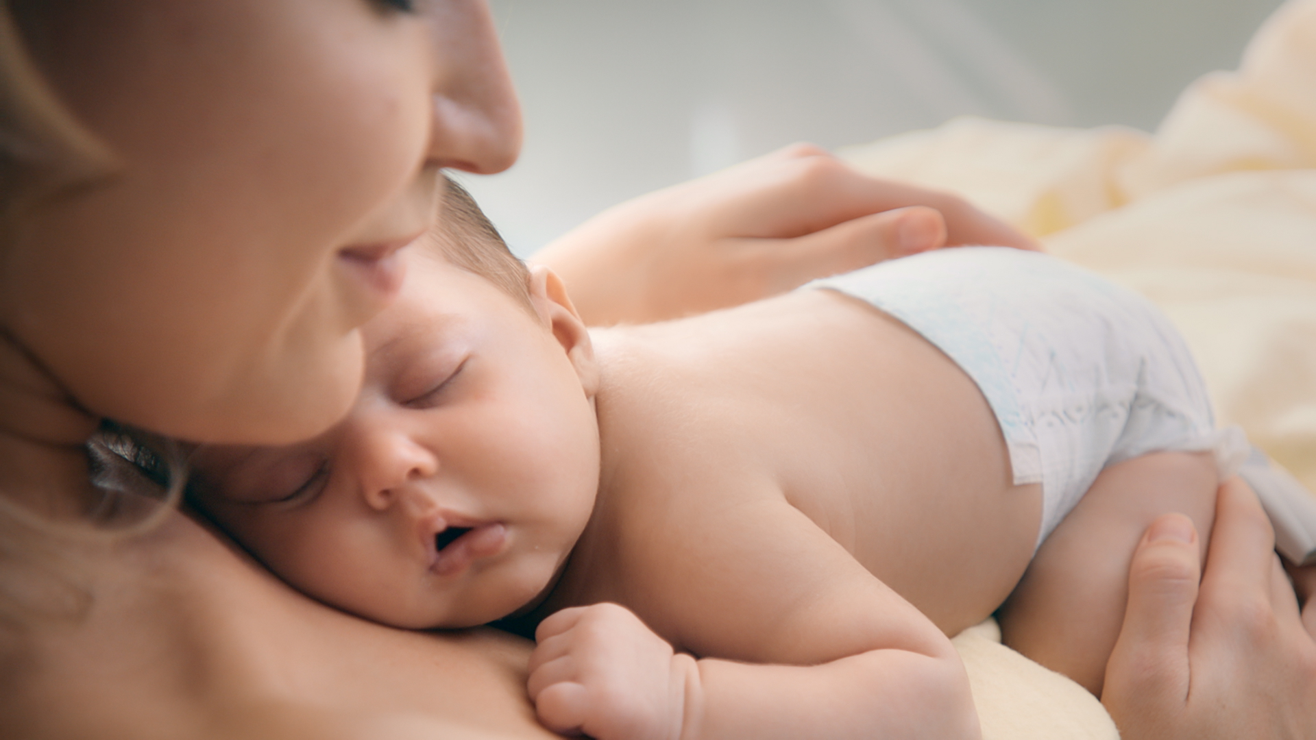 Nyugodt újszülött alszik édesanyja mellkasán, Pampers Premium Care pelenkát viselve