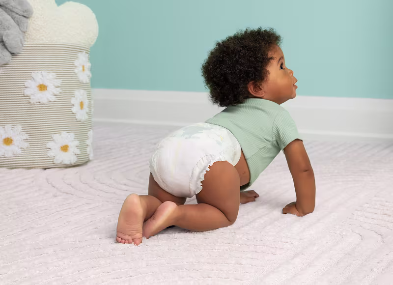 Baby crawling away on their nursery floor while wearing Pampers Swaddlers Ultra and a green shirt