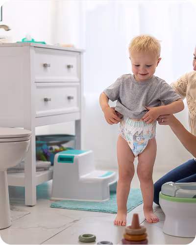 Mom helping her smiling son pull up a fresh Easy Ups training pant in the bathroom as he starts his potty training journey
