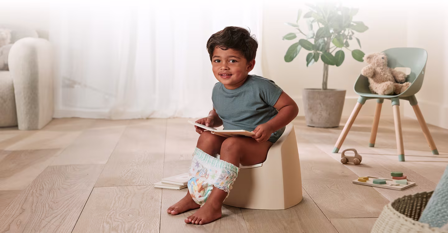 Un copil mic stă pe un oliță colorată într-o cameră luminoasă.