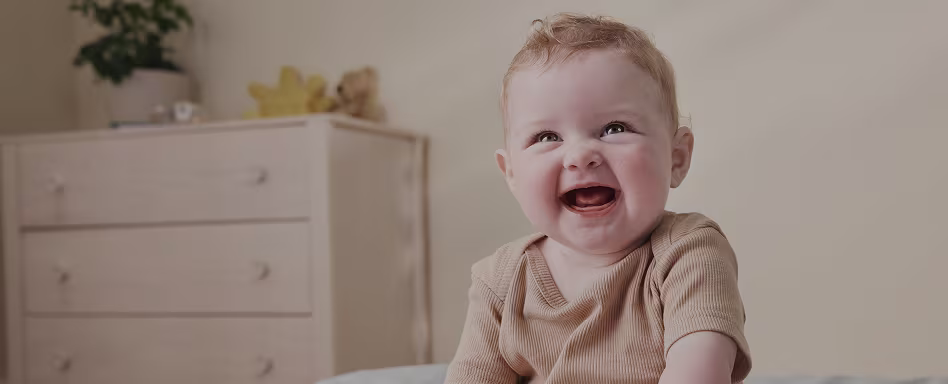 A closeup of a baby sitting in a children’s room smiling and looking at the camera