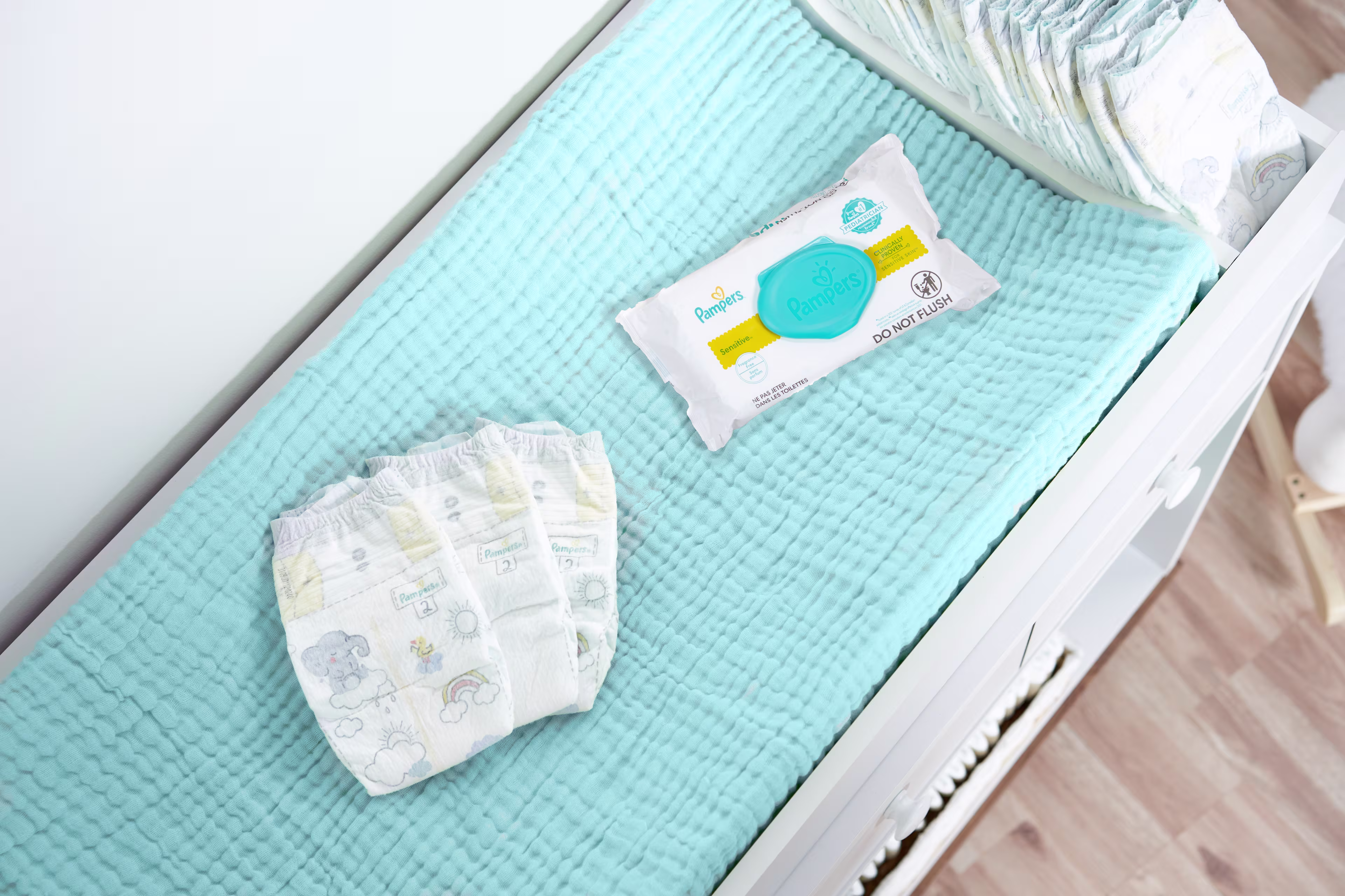 Swaddlers diapers and a Pampers Sensitive wipes pack on a changing table.