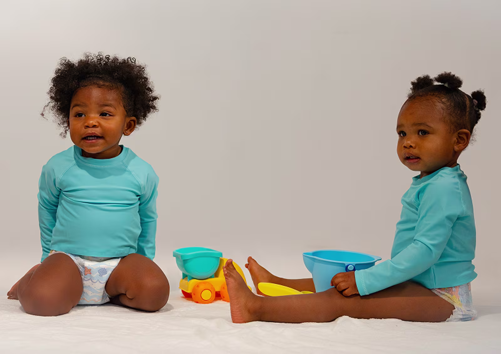 Deux tout-petits portant des Pampers Splashers sont assis ensemble avec quelques jouets de sable colorés.